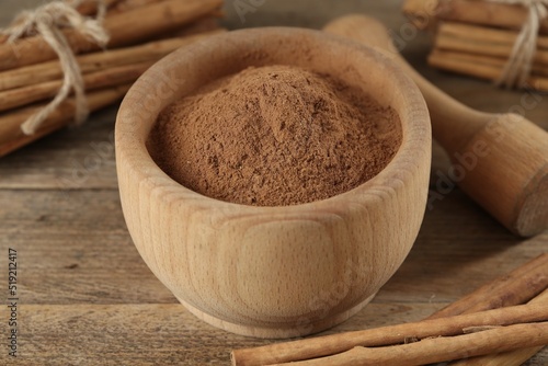 Aromatic  cinnamon powder in mortar, sticks and pestle on wooden table, closeup photo