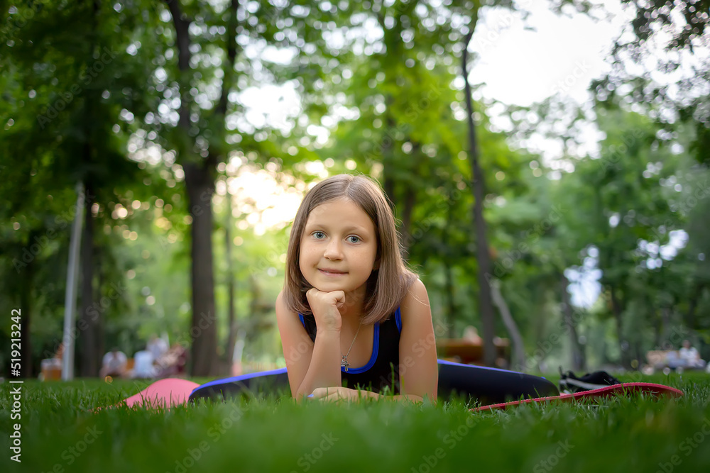 in the park, a little girl performs a frog element, doing stretching on a mat in the park, a little girl performs a frog element, doing stretching on a mat