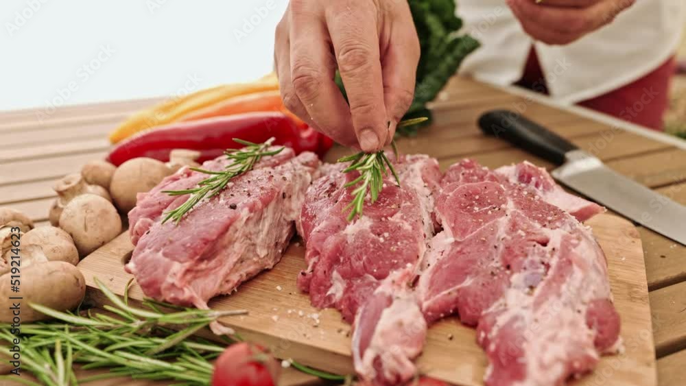 The chef carefully places the sprigs of rosemary on the juicy meat ready for the grill. The chef carefully places the sprigs of rosemary on the juicy meat ready for the grill.