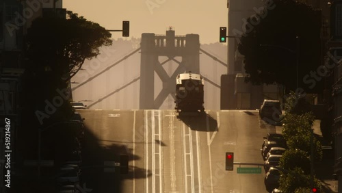 California street district in San Francisco, USA with historic tram riding up hill with Bay Bridge on background. RED camera shot of San Francisco hills on golden hour with cinematic morning sunlight photo