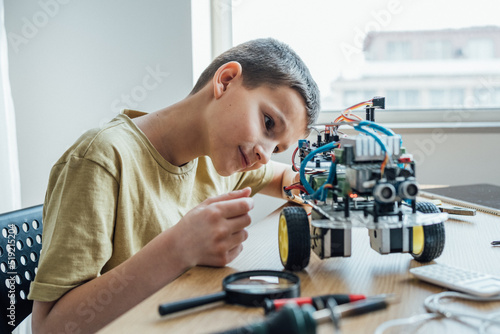 Concentrated boy building electronic robot while looking attentively on it at home. Education, science, hobby, leisure concept