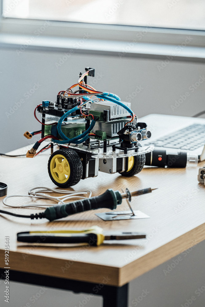 Vertical shot of the robot standing at the table with laptop computer and screwdriver. Programming,, science, technologies, DIY and science for kids concept Vertical shot of the robot standing at the table with laptop computer and screwdriver. Programming,, science, technologies, DIY and science for kids concept