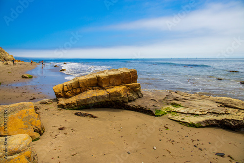 a gorgeous summer landscape at the beach with large rocks in silky brown sand surrounded by blue ocean water and waves rolling into the beach with blue sky and clouds at sunset at Leadbetter Beach photo