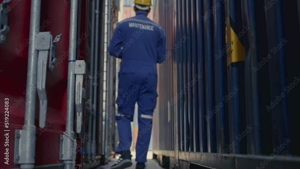 Full shot of Asian man maintenance shipping worker walking from camera checking container stack at container yard. Full shot of Asian man maintenance shipping worker walking from camera checking container stack at container yard.