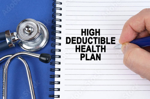 On a blue surface lies a stethoscope and a notebook in which it is written by hand - High Deductible Health Plan photo