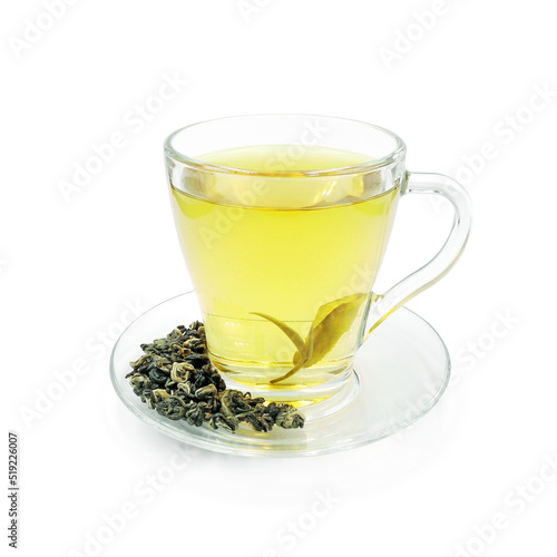 Green tea in glass cup on transparent saucer with scattering dry tea leaves isolated on white background 