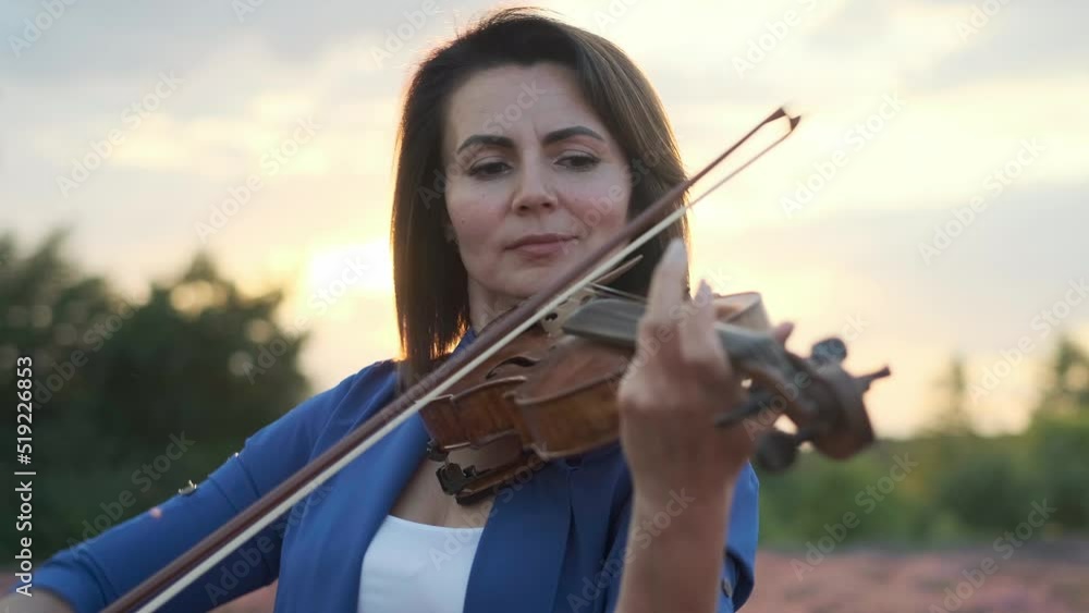 Woman playing violin at sunset. High quality 4k footage. Professional female musician playing violin and looking at camera against sundown sky in countryside. Woman playing violin at sunset. High quality 4k footage. Professional female musician playing violin and looking at camera against sundown sky in countryside.