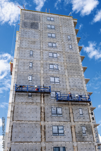 Builders, installers, high-rise workers, industrial climbers, plasterers on the lift, cladding of the facade of the building, completion of the construction of a residential building