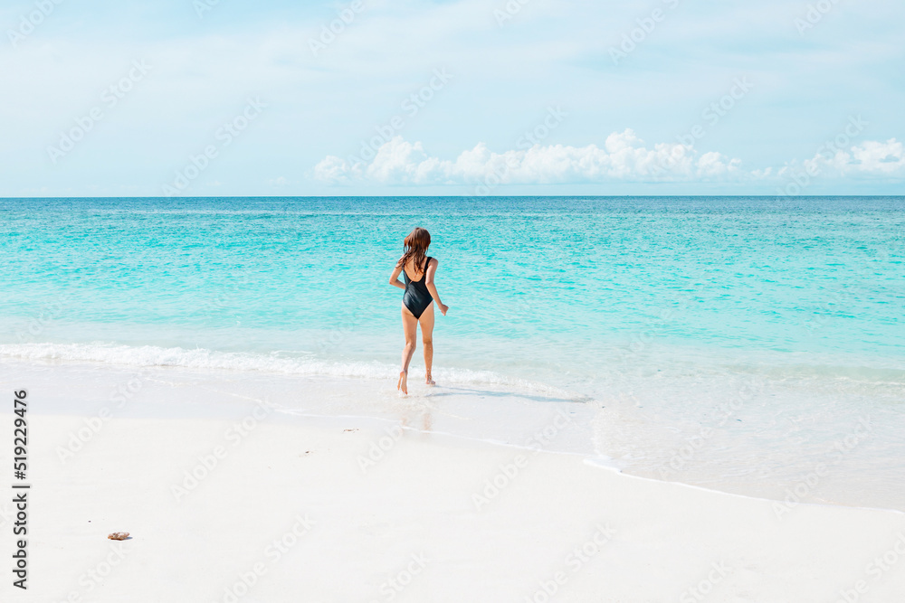 teenage girl with red hair in swimsuit run along the beach in the Maldives, a travel concept