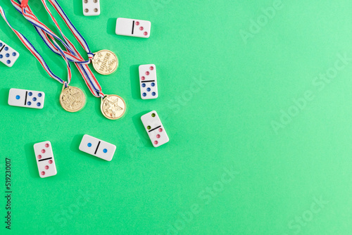 White dominoes with colorful dots and winner medals on a green background, top view. Board game.