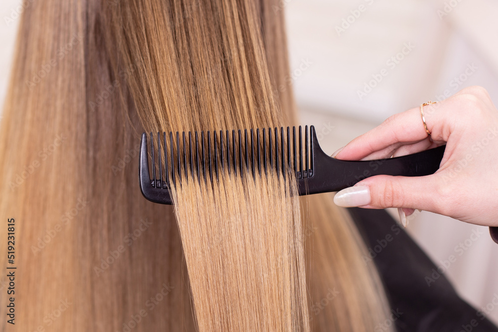 Fototapeta premium Hairdresser's hand brushing long natural blonde hair in beauty salon