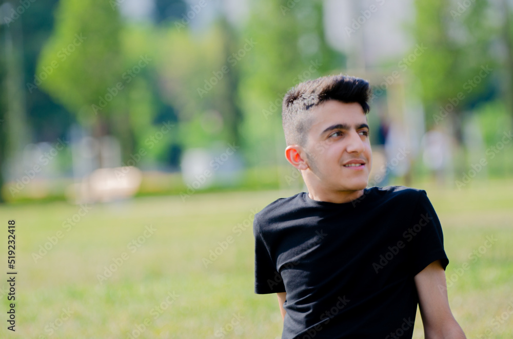 Handsome young boy in black shirt. Happy young male smiling on the grass in the park.