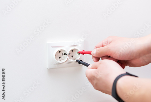 Measuring the voltage in the socket with a professional digital multimeter. Profession electrician, the process of installing sockets. Close-up, selective focus, noise.
