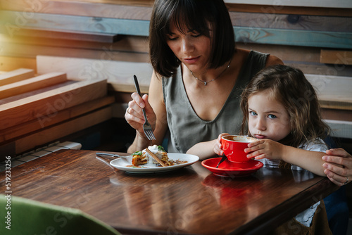 Tablou pe pânză Mom is sitting in a cafe with her ten year old daughter, she is eating a pie