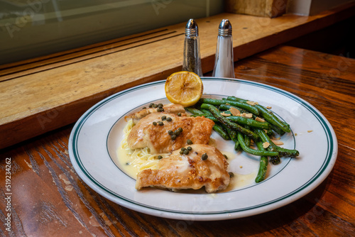 selective focus on chicken piccata with pasta and green beans on a white plate sitting on a rustic wood table by a window photo