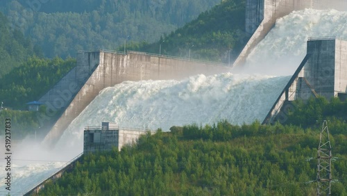 Coastal spillway of Sayano-Shushenskaya Dam on Yenisei River surrounded by forests. Passage for surplus water from hydroelectric plant. Landscape with artificial waterfall, wooded hills. Green energy