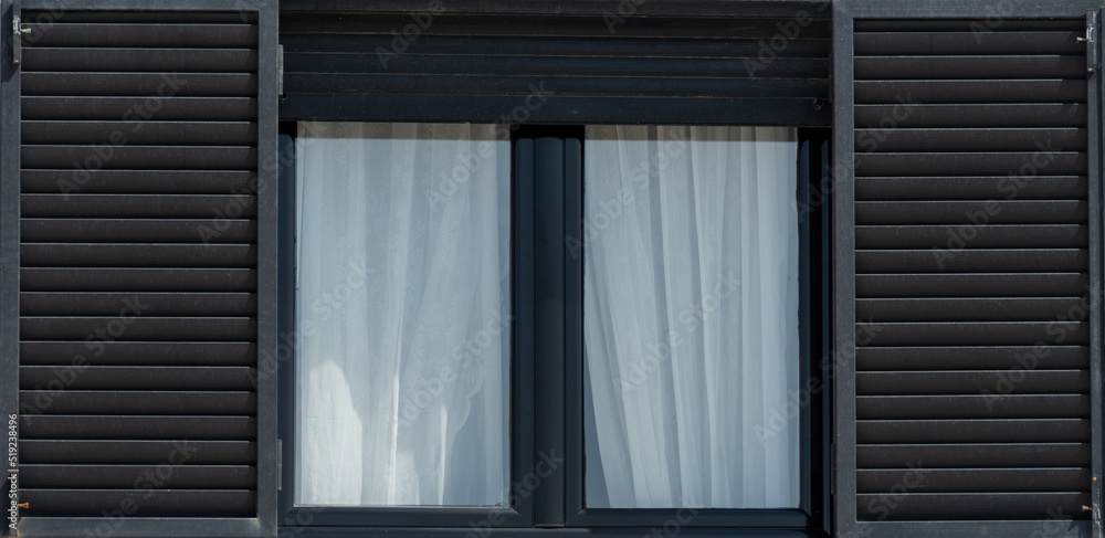 Fototapeta premium Frame of a wooden black window with white curtain and open shutters