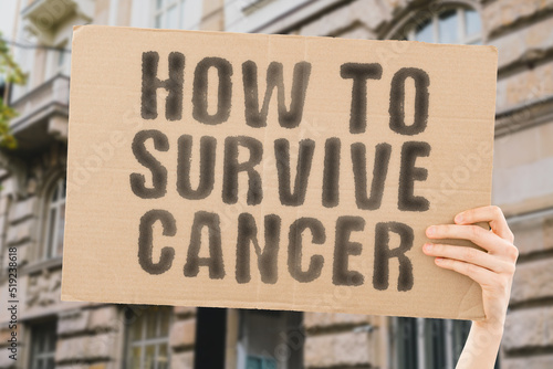 The phrase " How to survive cancer " is on a banner in men's hands with blurred background. Sick. Skin. Stomach. Therapy. Chemotherapy. Body. Care. Biology. Courage. Colon. Biotechnology. Beat