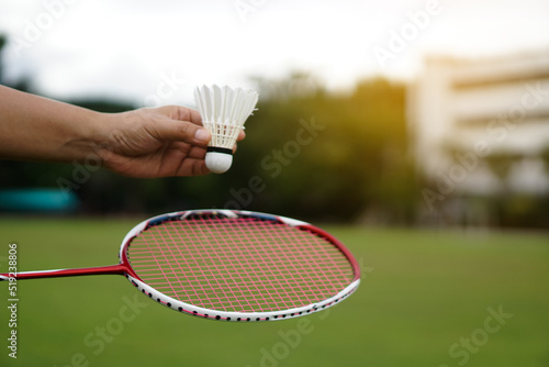 Hand holds shuttlecock for playing badminton outdoors.   Concept : Sport with equipment, workout. Recreational sport that can be played for fun or exercise and competition in team or individual.       photo