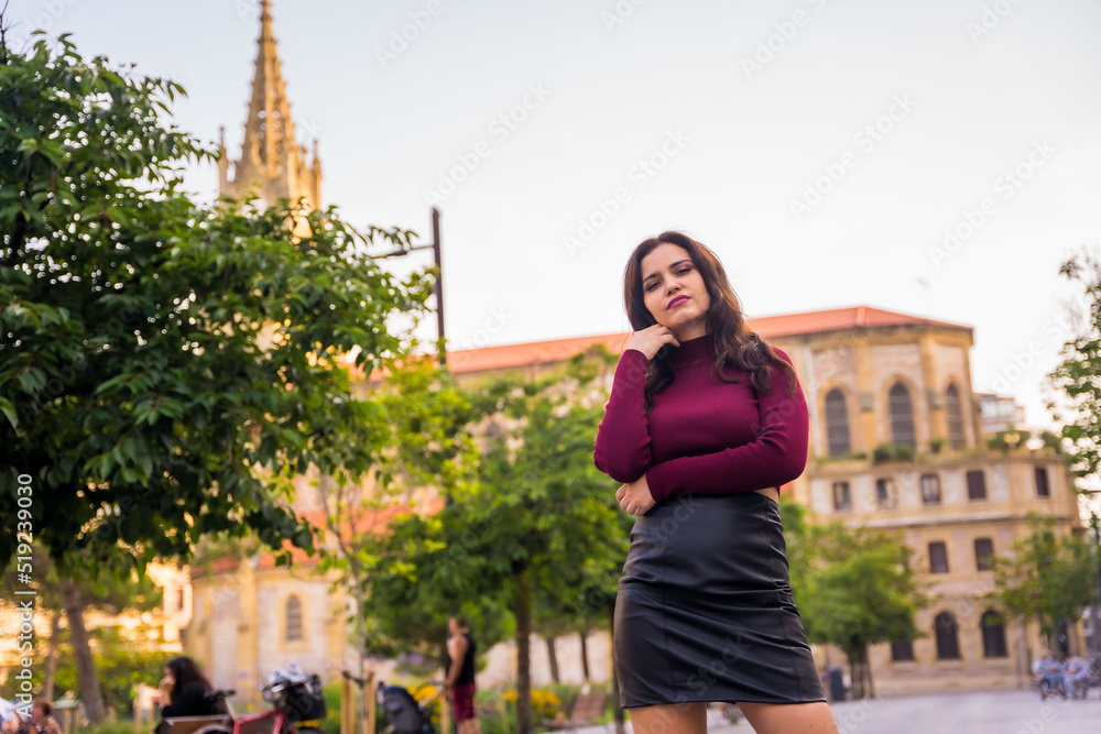 Portrait of a brunette woman with a leather skirt next to a church visiting the city, lifestyle