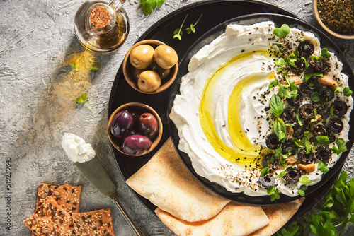 Arabic Cuisine: Middle Eastern delicious dip "Labneh". Cream cheese dip with olive oil, herbs and olives served with traditional pita bread. Top view with copy space.
