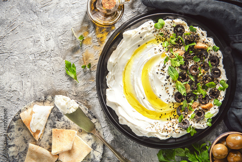 Arabic Cuisine: Middle Eastern delicious dip "Labneh". Cream cheese dip with olive oil, herbs and olives served with traditional pita bread. Top view with copy space.
