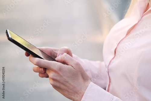 Beautiful business woman in a shirt near the panoramic window of the business center  typing text messages using a mobile phone. Close-up  side view