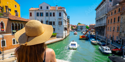 A woman with a hat standing on a bridge in Venice on a sunny summer and holiday day. © Damian