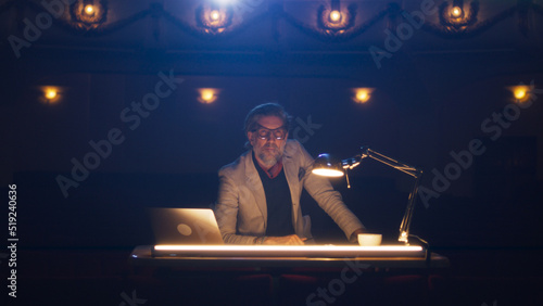 Photos The director in glasses and in a suit sitting at a table in a dark theater and t