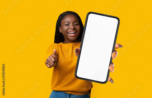 Positive Black Woman Showing Smartphone And Gesturing Thumb Up, Mockup © Prostock-studio