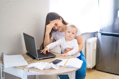 Young woman working at home with a laptop with a baby on his hands. Stay home concept. Home office with kids. Mother is working from home.