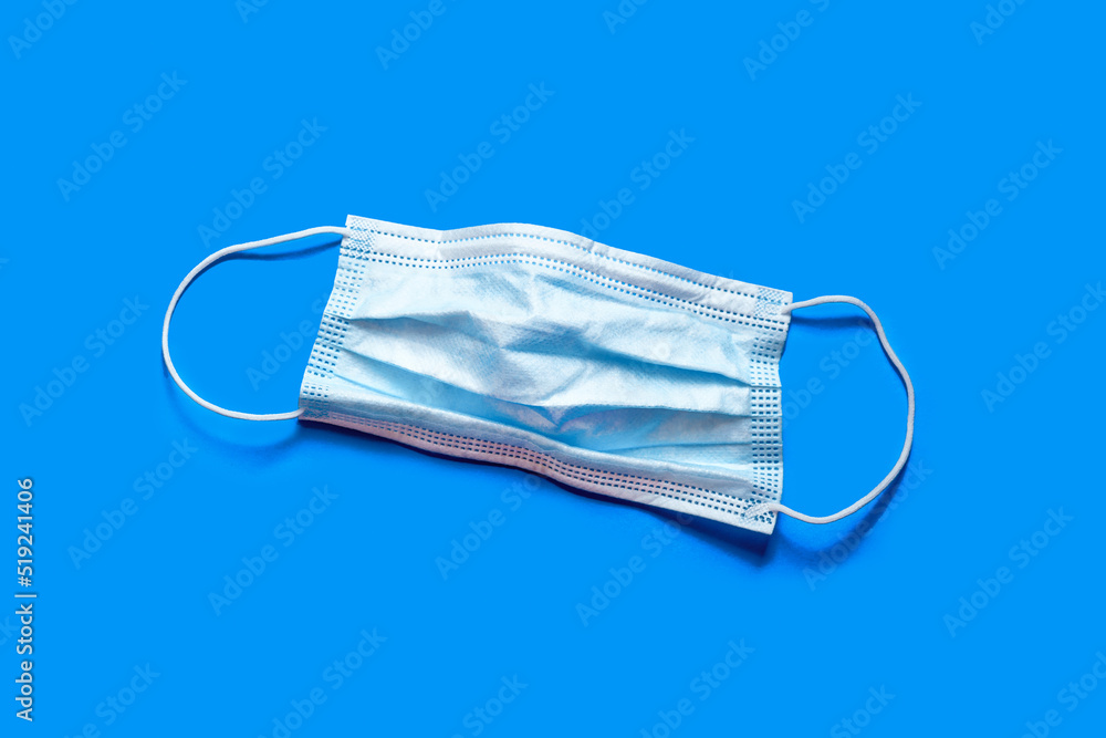 Disposable medical mask. Isolate on a blue background. Danger of viral infection. Protection against respiratory infection Disposable medical mask. Isolate on a blue background. Danger of viral infection. Protection against respiratory infection