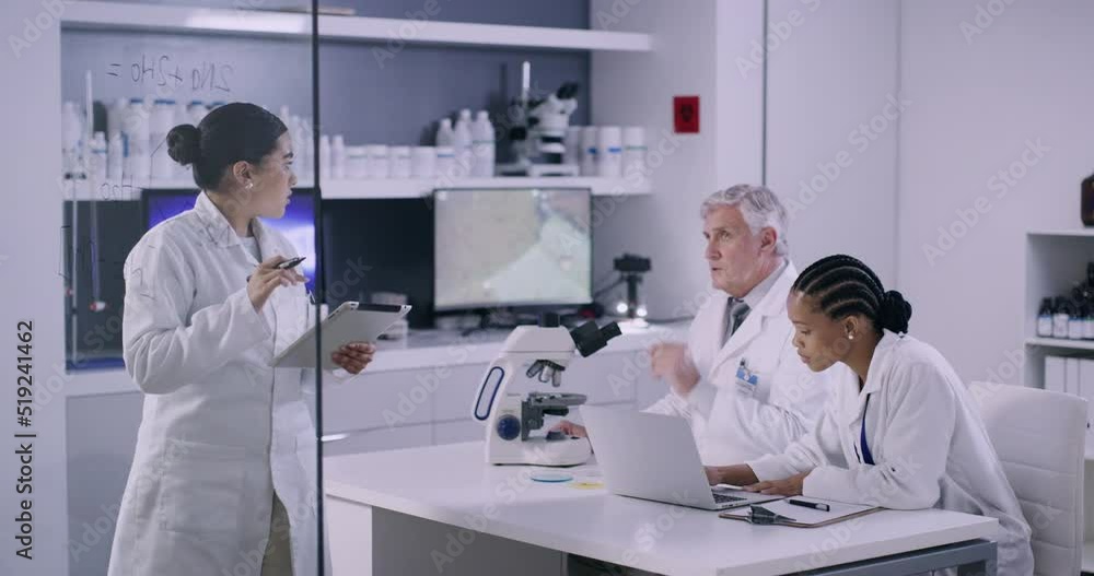 Team of scientists in a medical research lab discussing a chemical formula for a vaccine. Female researcher writing on a glass wall with colleagues working at a table in a modern laboratory Team of scientists in a medical research lab discussing a chemical formula for a vaccine. Female researcher writing on a glass wall with colleagues working at a table in a modern laboratory