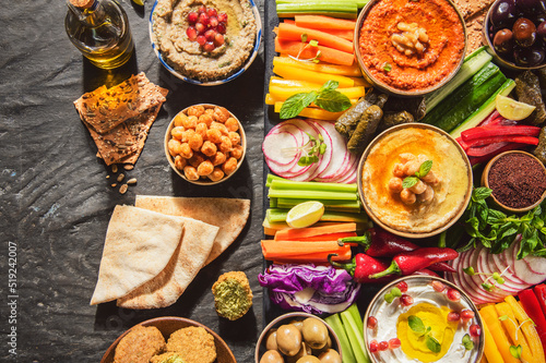Arabic Cuisine; Middle Eastern meze platter with green falafel, pita bread, vegetables sticks, olives, hummus, muhammara, baba ghanoush, , labneh, crackers and dolma . Top view with copy space.
