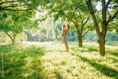 The joy of motherhood. Mom and daughter in the cherry orchard. Sunbeams on a green meadow © watman