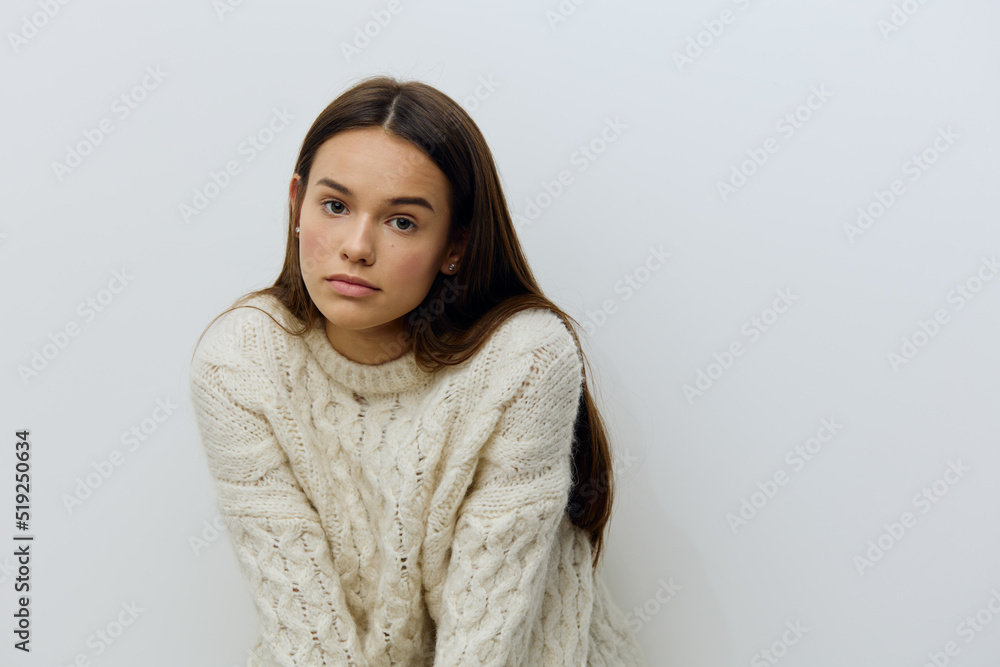 a young, beautiful, sophisticated woman stands in a warm white knitted sweater on a light background and looks pleasantly into the camera, leaning towards her. Horizontal photo with empty space a young, beautiful, sophisticated woman stands in a warm white knitted sweater on a light background and looks pleasantly into the camera, leaning towards her. Horizontal photo with empty space