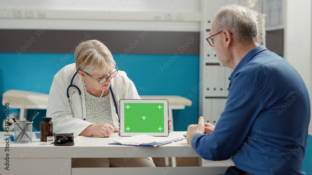 Senior physician pointing at tablet with horizontal greenscreen in medical cabinet. Using isolated copyspace background and blank chroma key template with mockup on display. Tripod shot. Senior physician pointing at tablet with horizontal greenscreen in medical cabinet. Using isolated copyspace background and blank chroma key template with mockup on display. Tripod shot.