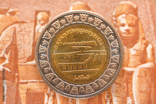 New Asyut city barrage project slogan from the obverse side of 1 LE EGP coin one Egyptian pound money on a blurred background of reverse side of one pound banknote cash money, selective focus photo