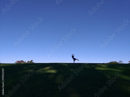 Girl dance poses with her arms up high on a hill against a blue sky