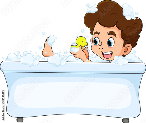 The happy boy is taking a bath in the bathtub and playing the duck rubber
