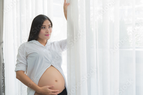Young mother or pregnant woman standing near window in living room at home Free Download Young mother or pregnant woman standing near window in living room at home - GFXLoad