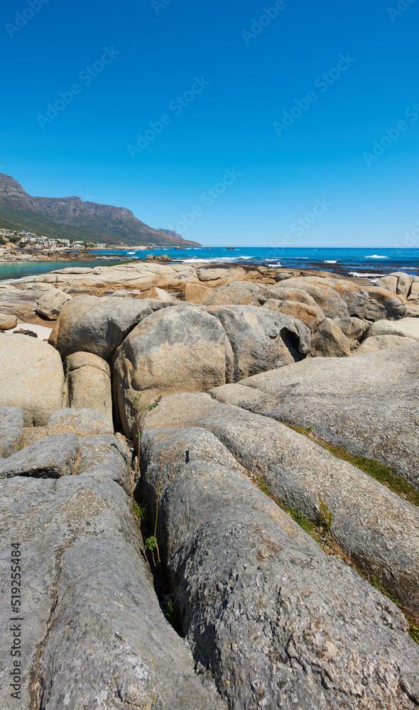Landscape, scenic and copyspace view of rocks and boulders on the seaside or coast against a clear blue sky in summer. Beautiful, peaceful and calm natural environment at the beach with copyspace