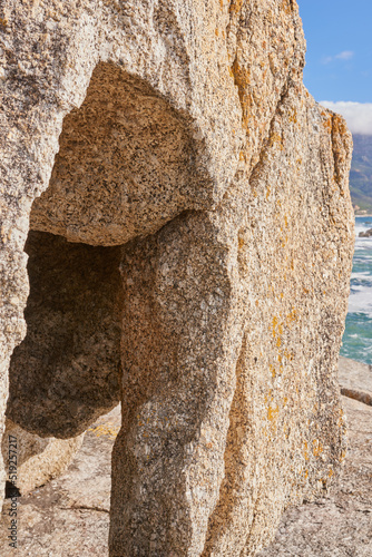 Closeup of a crevice or gully formed by the erosion of sea water. Large boulder or sandstone on a beach with the ocean in the background. Sedimentary rock acting as wave breaker on coastal seaside