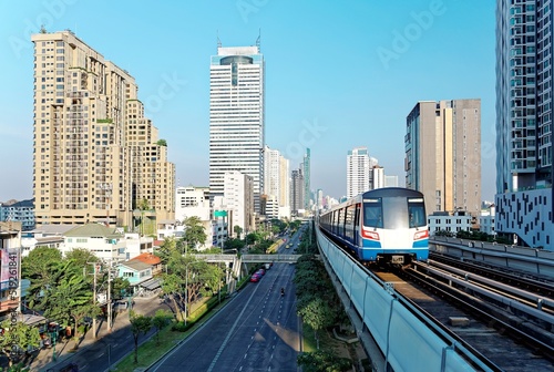 Cityscape of Bangkok, the fast developing capital city of Thailand, with view of a BTS skytrain traveling on an elevated metro system between high rise skyscrapers in downtown on a beautiful sunny day