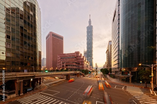 Cityscape of Downtown Taipei, the capital city of Taiwan, with 101 Tower & World Trade Center standing in XinYi Financial District at sunrise and cars dashing thru the intersection in morning twilight