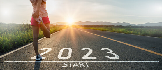 New year 2022 or start straight concept.word 2022 written on the asphalt road and athlete woman runner stretching leg preparing for new year at sunset.Concept of challenge or career path and change.