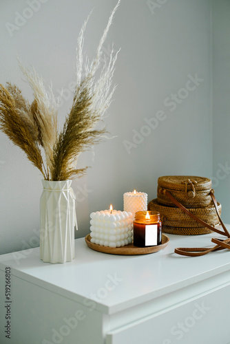 Home interior decor in beige neutral colors. White dresser with dried flowers in vase, rattan bags and candle. Mockup concept