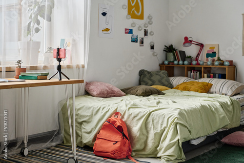 Horizontal image of teenage room with cozy bed and table with smartphone on tripod photo