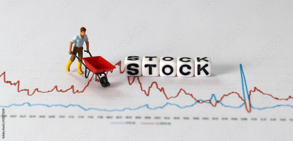 Business concept with graphs and miniature people. White cube with 'STOCK' text.
