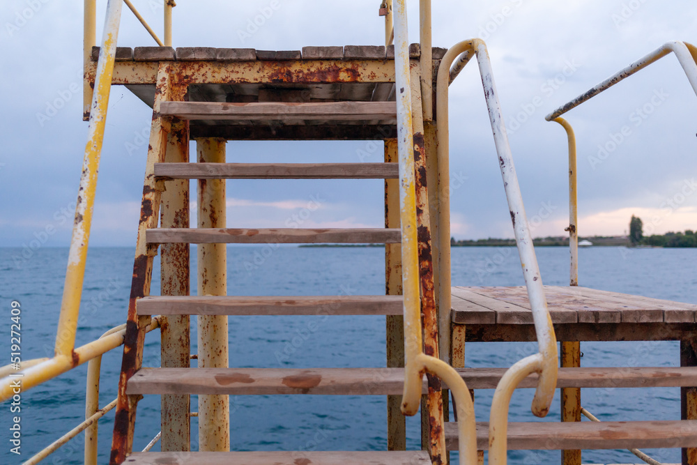 large pier with a roof and a rusty staircase descending into the water large pier with a roof and a rusty staircase descending into the water